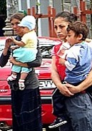 Zwei Roma-Mtter mit (ihren???) Kindern auf dem Arm betteln. Hinter ihnen steht ihr Fahrzeug, in dem sie wechselseitig ausruhen ...